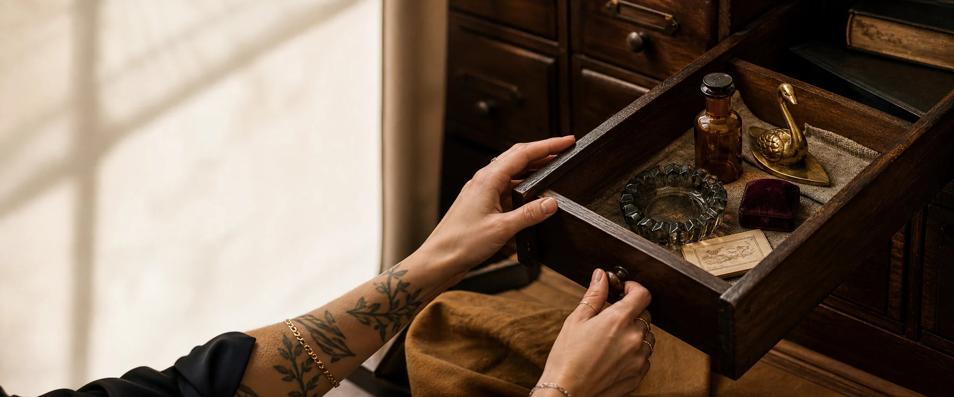 Les mains tatouées de Stéfani ouvrant un tiroir ancien rempli d’objets choisis